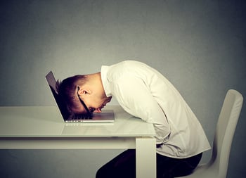 Man leaning over desk with head on laptop